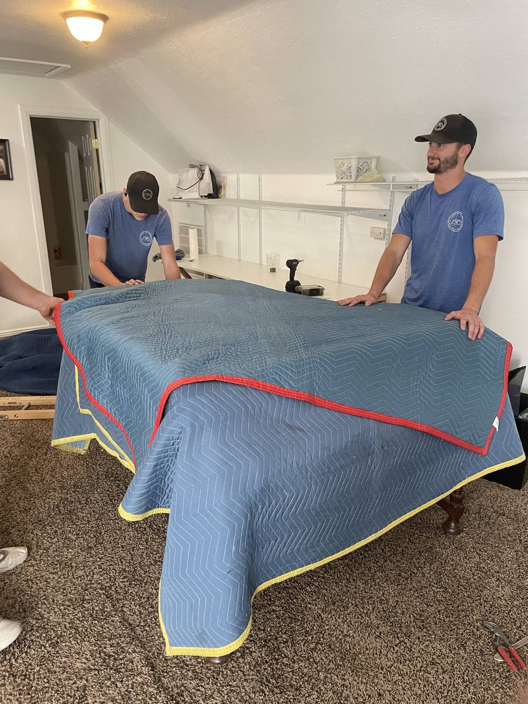 Two movers wrapping a grand piano in a padded moving blanket before transport